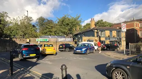 A busy road junction in Leeds with a lot of vehicles trying to turn left or right, and a pedestrian crossing.