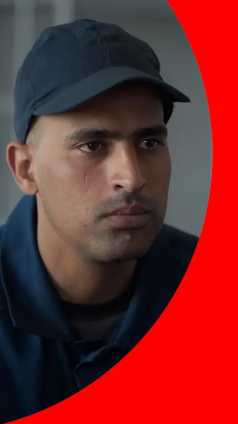 A man, Khalil wears a navy blue prison uniform and cap.