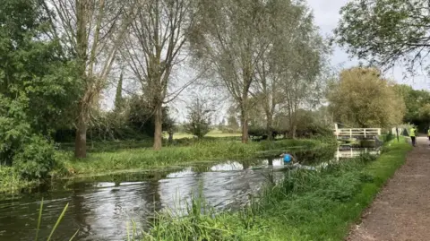 Canal & River Trust The Bridgwater and Taunton Canal seen from the footpath. There is a kayak on the canal and people are walking further ahead.