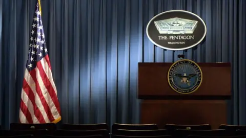 Pentagon press room with empty podium under Pentagon sign next to American flag