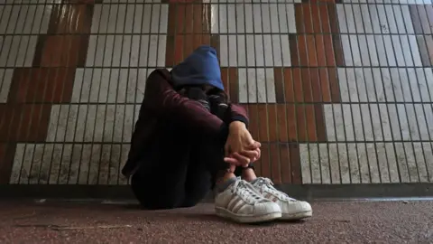 PA Media Library shot of child wearing blue hood sitting next to a wall