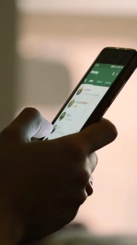 Close-up of a hand holding a smart phone. The screen of the phone is lit and the hand is in silhouette