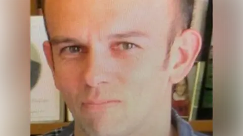 New Zealand police officer Tom Phillips is pictured with a close-up on his face. He looks directly into the camera with a neutral facial expression. 