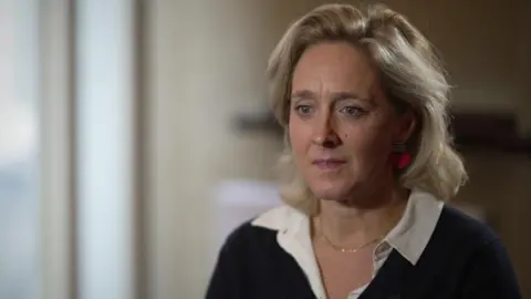 Kate Pakenham, producer of Punch, wearing a white blouse, gold chain and black cardigan sitting down