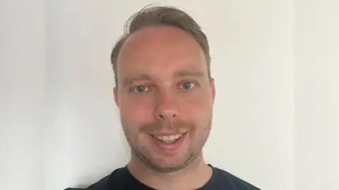 Gloucestershire Hospitals NHS Trust Liam Ward smiling against a white wall