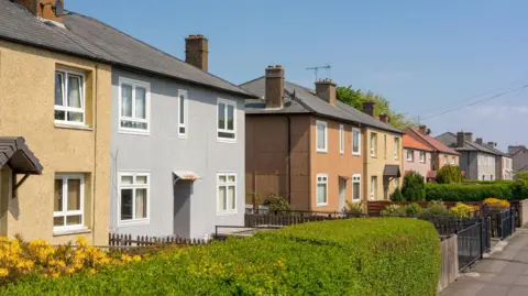 A street of colourful houses beside a road with hedges under a clear blue sky