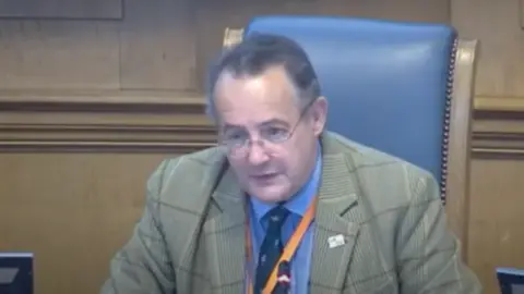 Wiltshire Council Councillor Paul Sample sits in the Wiltshire Council chamber addressing other members.