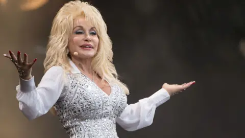 Dolly Parton dressed in a sparkly white outfit while on stage at Glastonbury in 2014.