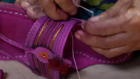 A women threads a needle through a leather Kolhapuri slipper in a workshop in Kolhapur, Maharashtra