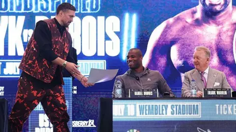 Oleksandr Usyk hands Daniel Dubois a picture to sign