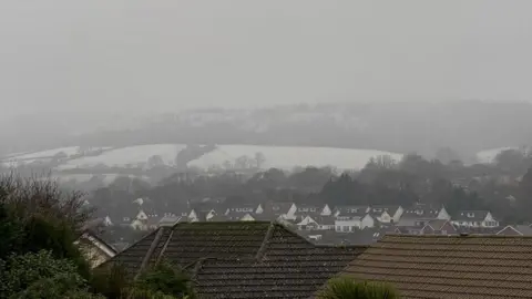 Amanda O'Carroll Snow seen in the fields across Sidmouth, there are rooftops which are dry of snow but fields behind it covered