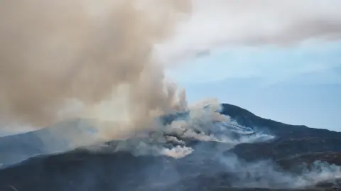 Smoke billowing out from a mountain, filling the sky