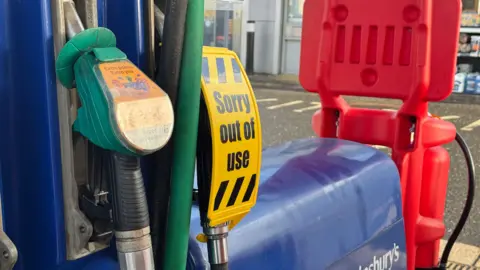 A 'sorry out of use' sign over a fuel pump in a supermarket forecourt 