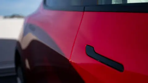 Bloomberg via Getty Images A black door handle on a red Tesla Model Y at a charging station in San Francisco, California, US.