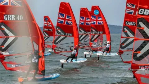 Bill McCandlish A fleet of Great Britain branded windsurfing boats they have bright red sails.