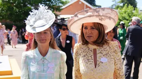 PA Media Carole Middleton (pictured on the right) arrives at Ascot with her daughter-in-law Alizee Thevenet. They are both wearing hats.