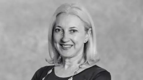 Metropolitan Police Black and white photo of Catherine Finnegan. She has shoulder length hair, wears earrings, a necklace, a black top and smiles at the camera.