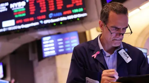 Getty Images Trader on floor of New York Stock Exchange with red seen on the board behind him