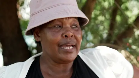 Head and shoulders shot of a woman weaking a light pink bucket hat and white cardigan over a black top.