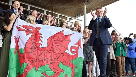 Rhun ap Iorwerth surrounded by his fellow Plaid Cymru Senedd members on the steps of the Welsh Parliament building.