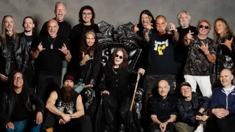 Ross Halfin More than a dozen singers and band members from many legendary groups join Ozzy for a group photo. He is seated in the centre, with everyone, pretty much all wearing black, surrounding him.