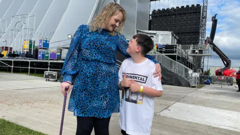 Danny Fullbrook/BBC Josh and his mum smiling at each other behind the main stage at the festival