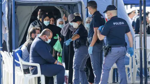 Italian police officers check immigrants just disembarked from a rescue ship