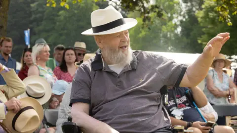 Gorman Photography Michael Eavis is waving from his wheelchair to the crowd.