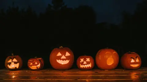 Getty Images A row of various sized carved Halloween pumpkins with different facial expressions glowing in the dark.