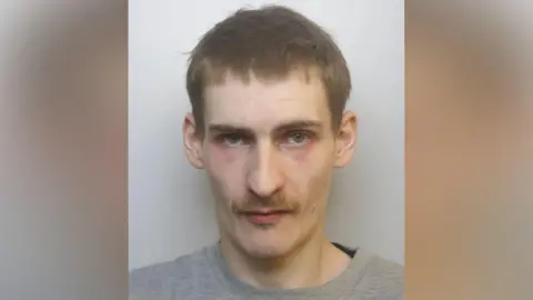 Avon and Somerset Police A mugshot of Gunter. He is looking at the camera with a neutral expression. He is wearing a grey jumper, and has a mustache and short brown hair. He has red marks under his eyes.