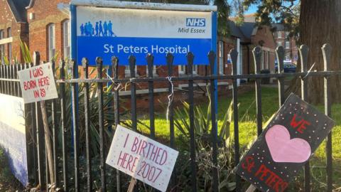 The St Peter's Hospital sign in the background, and protest placards in the foreground
