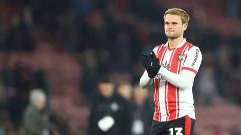 Getty Images Léo Scienza wearing a red and white saints kit and applauding the fans.