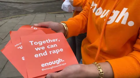 The hands of a woman holding orange leaflets that says 'Together, we can end rape'