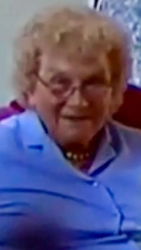Burton on Stather Heritage Group Sally Robinson - a woman in her 80s with glasses - smiles at the camera. She is sitting on a sofa and wearing a short-sleeved, lilac blouse.