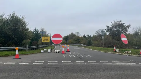 Tony Fisher/BBC One lane of the bypass is lined with two large 'no entry' signs: red circles with a horizontal white line in the centre. There are also cones that line the bypass along a line from the image font around the bypass until they are out of sight. A yellow sign with black words 