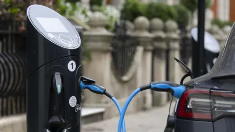 An electric car is charging at a socket next to a pavement.