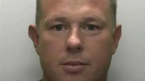 Devon and Cornwall Police A mugshot of Simon Mitchell who has pale short hair and blue eyes.