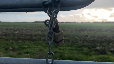 Close-up of a chain and lock on a gate which leads to a green farmer's field