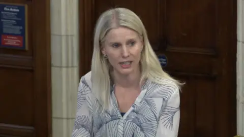 UK PARLIAMENT Rebecca Paul, the Reigate MP, talking in a debate at Westminster Hall in Parliament. She is wearing a white top with a blue pattern.