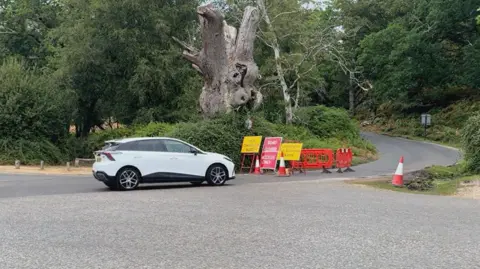 A white car approaches a road closure sign