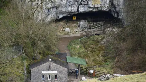 David Martin/Geograph Ingleborough caves seen from above: a stone building and a gate at the end of a path which leads to some stone caves