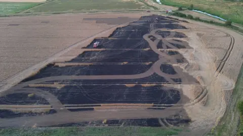 Dan Jessup An aerial image shows a large area of burnt farmland near Berwick. Extensive blackened ground stretches across the centre of a field. Vehicle tracks criss-cross the burnt area and several fire engines and vehicles are visible near the top of the field.