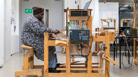 A woman with a blue and white patterned outfit sat at a loom weaving