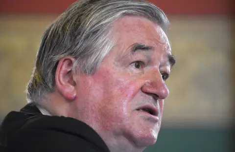 Pa media is close to the sides of the side of a person with gray hair. The background tried focus and looks inside the room with red, green, and beige color