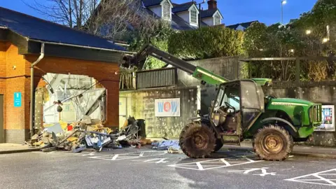 A telehandler next to a wall which has been ram-raided at a shop in Devon