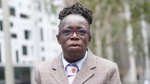 PA Media Ms Adoo-Kissi-Debrah in a suit jacket, pink tie and white shirt. 