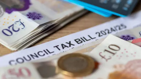 A council tax bill for 2024/25 is on a wooden table - there are pound notes and coins on top of the bill.