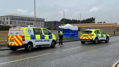 BBC a police van, car and two officers in the road outside an industrial estate