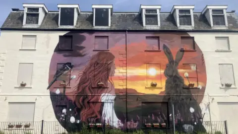 Mural on the site of the former Osborne hotel in Warrenpoint, featuring a woman an amber sky and a rabbit