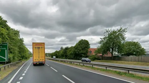 A dual carriageway on a cloudy day. Lorries and cars travel on each side of the road.